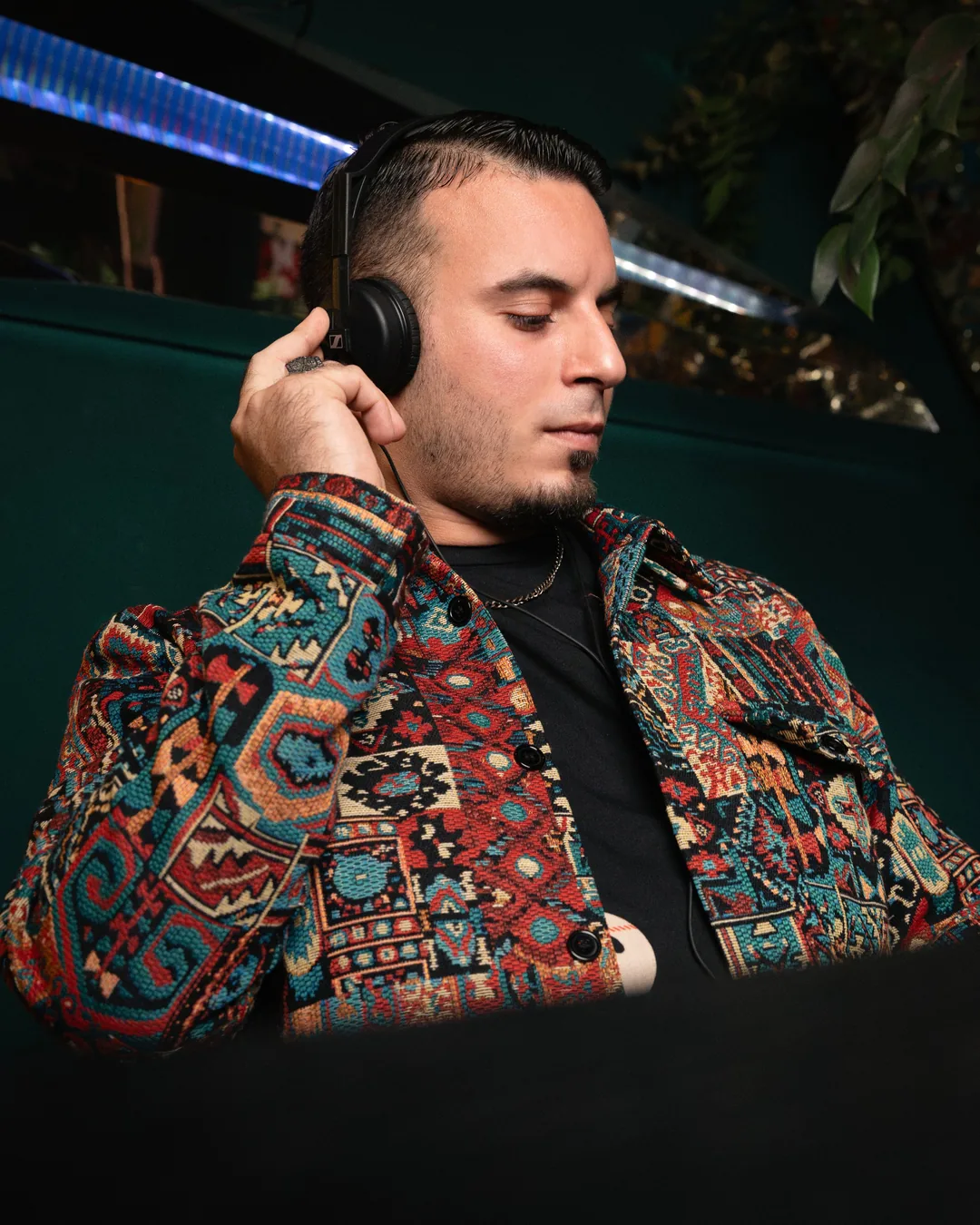Ein DJ mit Kopfhörern und gemusterter Jacke legt auf