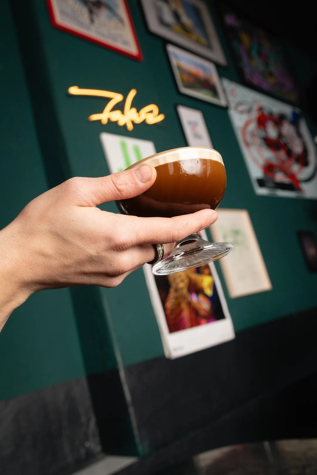 Eine Hand hält eine Coupe mit einem dunklen Drink
