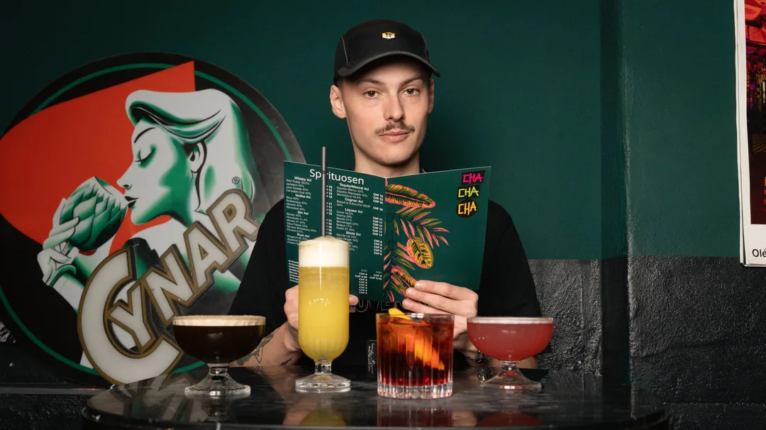 Ein Gast mit Mütze liest die Getränkekarte, vor ihm drei Drinks