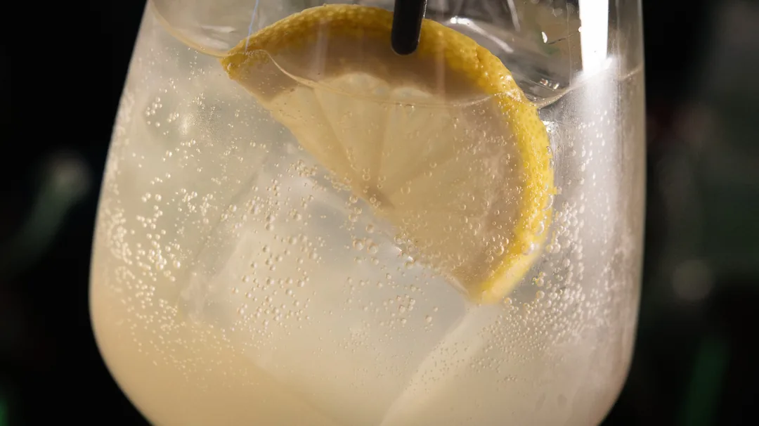 Ein heller Long Drink mit Zitronenscheibe und Eis